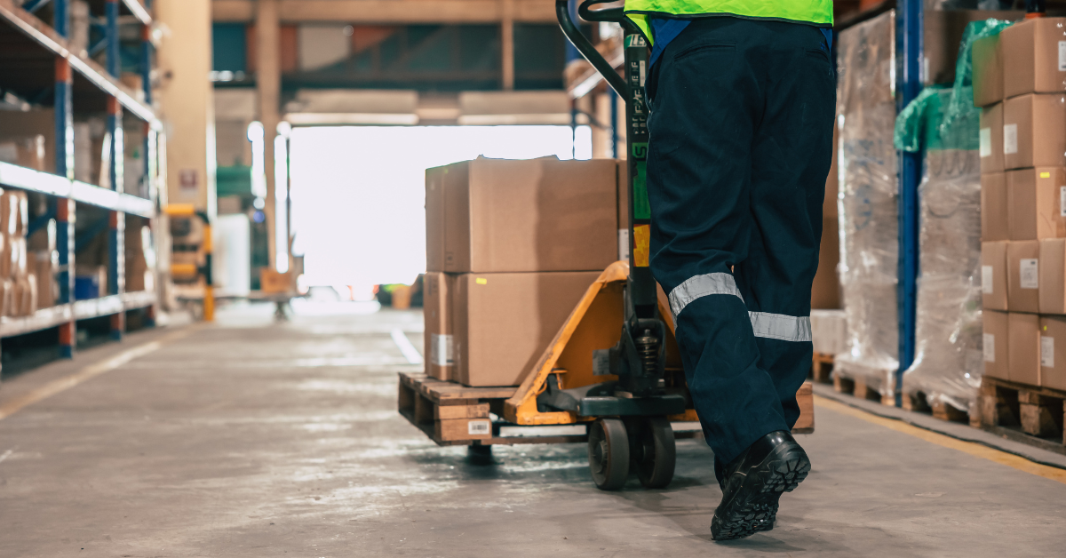 Warehouse worker pushing a manual pallet jack with deliveries.
